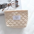 Detailed close-up of a quilted cream cosmetic bag with a minimalist woven brand label - Embossed Apricot Diamond