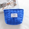 Close-up of blue quilted waterproof nylon makeup bag with white label and zip closure - Quilted Vertical Stripe Royal Blue