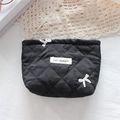 Close-up of black quilted cosmetic bag featuring white bow embroidery and logo tag - Black Embroidered Bow