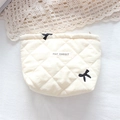 Detail of quilted cosmetic bag with black bow embroidery and woven brand label - Cream Embroidered Bow