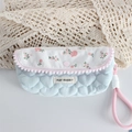 Macro detail of quilted heart pattern with floral flap and decorative pink pom-poms - Crinkled Fabric Blue Heart Floral Pencil Case