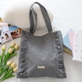 Détail du sac cabas à carreaux avec bords à volants et étiquette sur literie blanche - Carreaux Noirs