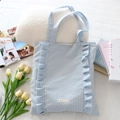 Dettaglio di una borsa tote in tela a quadretti blu con volant e logo su sfondo stile di vita - Quadri Blu