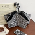Klassischer schwarz-weißer karierter Taschenschirm mit passender Hülle auf einem Holztisch - Schwarz Weiß Karo