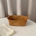 Detail of handwoven oval seagrass basket with sturdy handles on a white tabletop - Caramel Small
