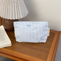 Blue and white striped bow cosmetic bag on a wooden desk with a vintage lamp - Blue Striped (01) / Small