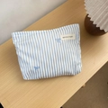 Detail of blue striped makeup bag with bow embroidery and logo on wooden surface - Blue Striped (01) / Large