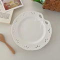 Dettaglio macro del piatto in ceramica bianca con bordo traforato e decoro a fiocco - crema