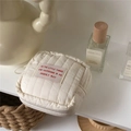 Close-up of a cream quilted square pouch with a pink text patch in a cozy setting - MINI Style