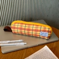 Detail van geel geblokt etui met stoffen handvat en rits op een houten bureau - Oranje Gingham