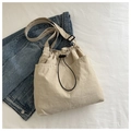 Detalle de bolso de lona crema con cordón y correa ajustable sobre fondo de denim - Caqui
