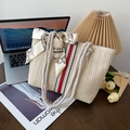 Beige geflochtene Strohtasche mit roten Streifen und Seidenschleife auf einem Schreibtisch - Weiß-Rot
