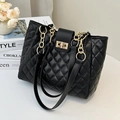 Sac fourre-tout matelassé noir avec chaîne dorée et fermoir rotatif sur une table blanche - Losange Noir