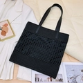 Schwarze gewebte Stroh-Tote-Bag mit Ledergriffen in einer stilvollen Modeszene präsentiert - Schwarz