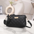 Black quilted cross body bag with gold hardware and adjustable strap on marble table - Black