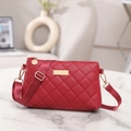 Red quilted crossbody bag with diamond texture and golden metal hardware on marble surface - Red