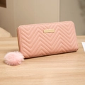 Pink quilted leather long wallet with zipper and fluffy ball keychain on wooden table - Pink