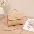 Pink straw crossbody bag with S logo and faux leather handle on wooden desk - Pink