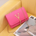Pink checkered crossbody bag with gold V logo, tassel detail, and chain strap on sofa - Rose Red