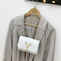 White quilted crossbody bag with golden deer charm and tassel on a grey blazer - White