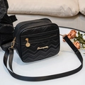 Chic black crossbody bag with V-shaped quilting and gold hardware on a white table - Black