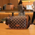 Brown checkerboard crossbody bag with golden logo and orange leather trim on wood - Brown