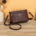 Quilted dark brown crossbody bag with gold logo on a rustic wooden table background - Burgundy