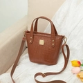Brown crocodile embossed bucket bag with gold hardware and adjustable strap in home setting - Brown