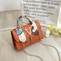 Orangefarbene Stepptasche mit Seidenschal-Griff und Quaste auf hellem Holzboden - Orangerot