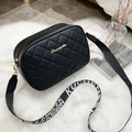 Chic black quilted crossbody bag with golden logo and patterned woven strap on plush background - Black