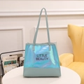 Green holographic tote bag with Little Beauty text and shoulder strap on white table - Blue