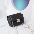 Black quilted crossbody bag with gold chain strap and metallic lock on marble surface - Black