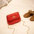 Mini red quilted crossbody bag with gold chain strap and turn-lock closure on bed - Red