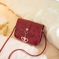 Burgundy embossed cartoon crossbody bag with pink heart pendant on soft white bedding - Red