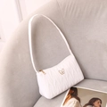 White quilted underarm bag with gold butterfly hardware on a stylish gray sofa - White