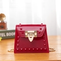 Red jelly bag with glossy rivets and gold chain strap on a wooden desk with vintage decor - Red