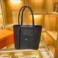 Minimalist black tote bag with lychee texture and gold button detail in a boutique display - Black