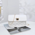 White quilted crossbody bag with gold heart clasp and metal chain on a magazine - White