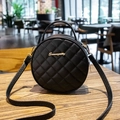 Borsa rotonda nera con motivo trapuntato, logo dorato e tracolla su tavolo in legno - Nero
