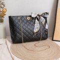 Black quilted tote bag with golden chain and decorative silk scarf on straw mat - Black