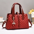 Elegante rote gesteppte Beuteltasche mit Kirsch-Anhänger und goldenen Details auf Tisch - Rot