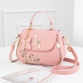 Elegant pink leather handbag with floral embroidery and pearl clasp on a white surface - Pink
