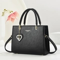 Bolso de mano minimalista en cuero negro con herrajes dorados y colgante de perla y corazón - Negro