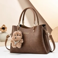 Elegant dark brown leather tote bag with gold logo and plush bear charm on beige background - Khaki