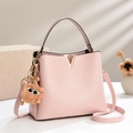 Minimalist light pink leather handbag with gold V-detail and plush charm on marble base - Pink