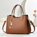 Sac à main classique en cuir grainé marron avec détails dorés et pompon sur fond blanc - Jaune Terre