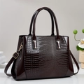 Close-up of deep wine red crocodile textured handbag with polished patent leather details - Brown