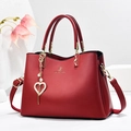 Bolso de mano elegante en cuero rojo con logo dorado, correa y colgante de corazón - Burdeos