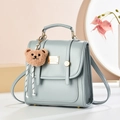 Minimalist light blue leather backpack with vertical straps and a brown teddy bear charm - Solid Color / Teal