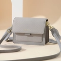 Light gray crossbody bag with textured flap and gold hardware on minimalist background - Gray